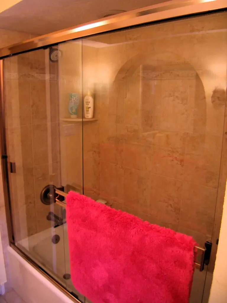 An updated shower with warm 18 inch tile, oil rubbed brinze fixtures, and a brass framed shower enclosure