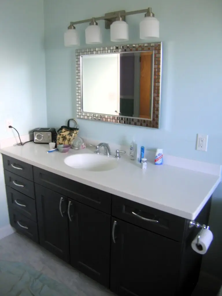 White countertops and a gray vanity with unique mirror for her