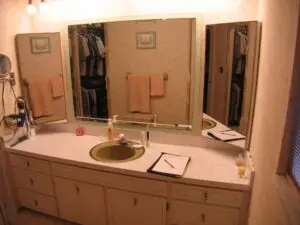 Before photo of a 1960s bathroom with a pink vanity and avocado green sink.