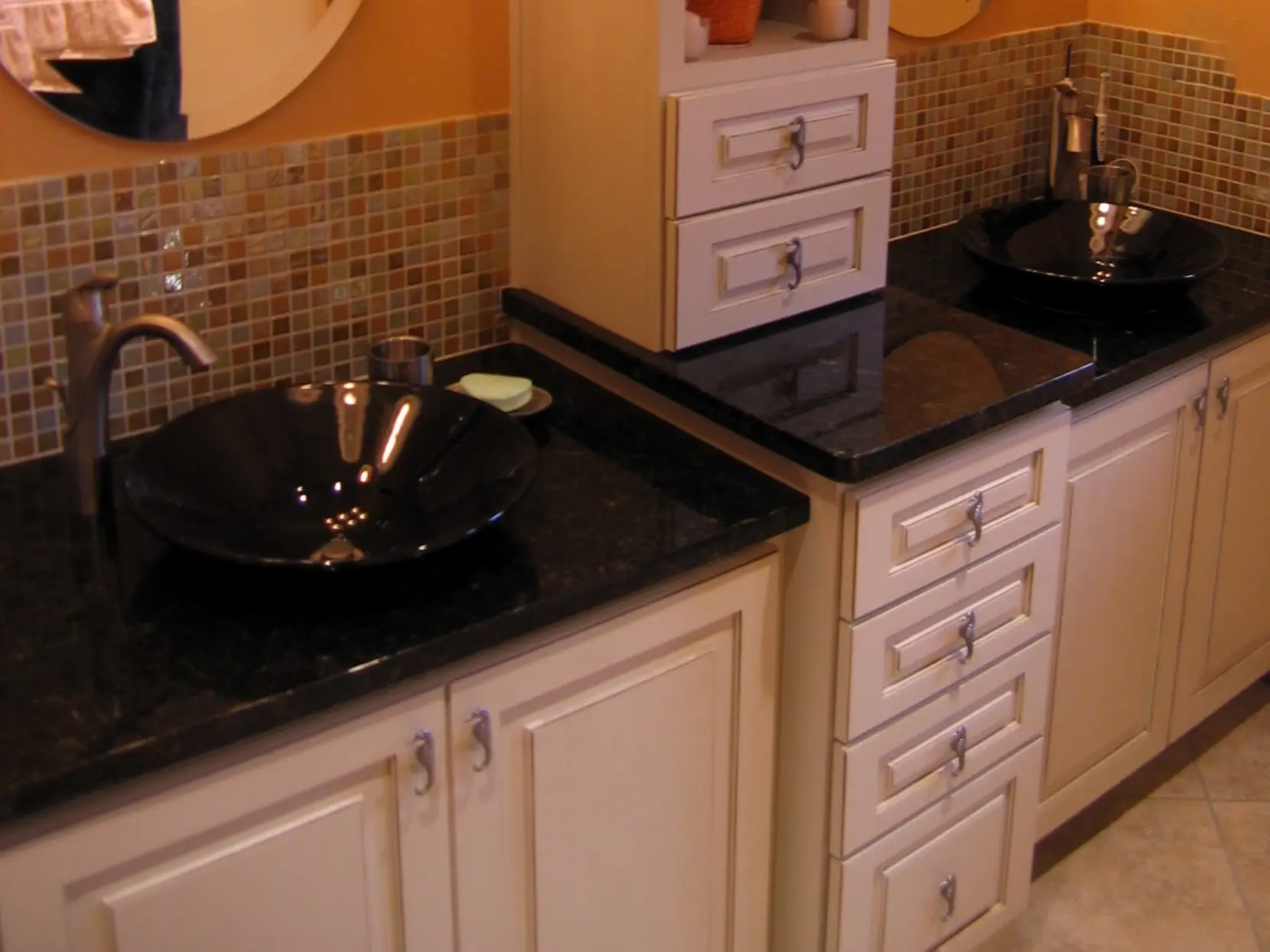 Close-up of a bathroom vanity with two black porcelain vessel sinks and black granite countertops