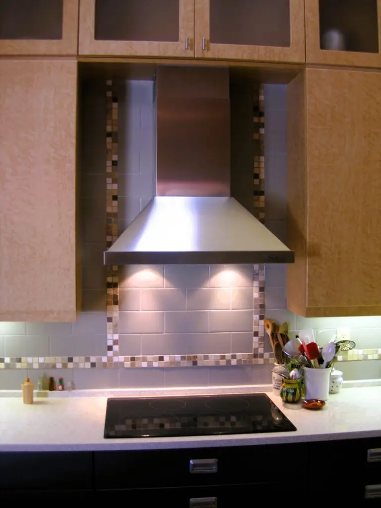 Earthtone mosaic tile backsplash framing stainless steel chimney hood