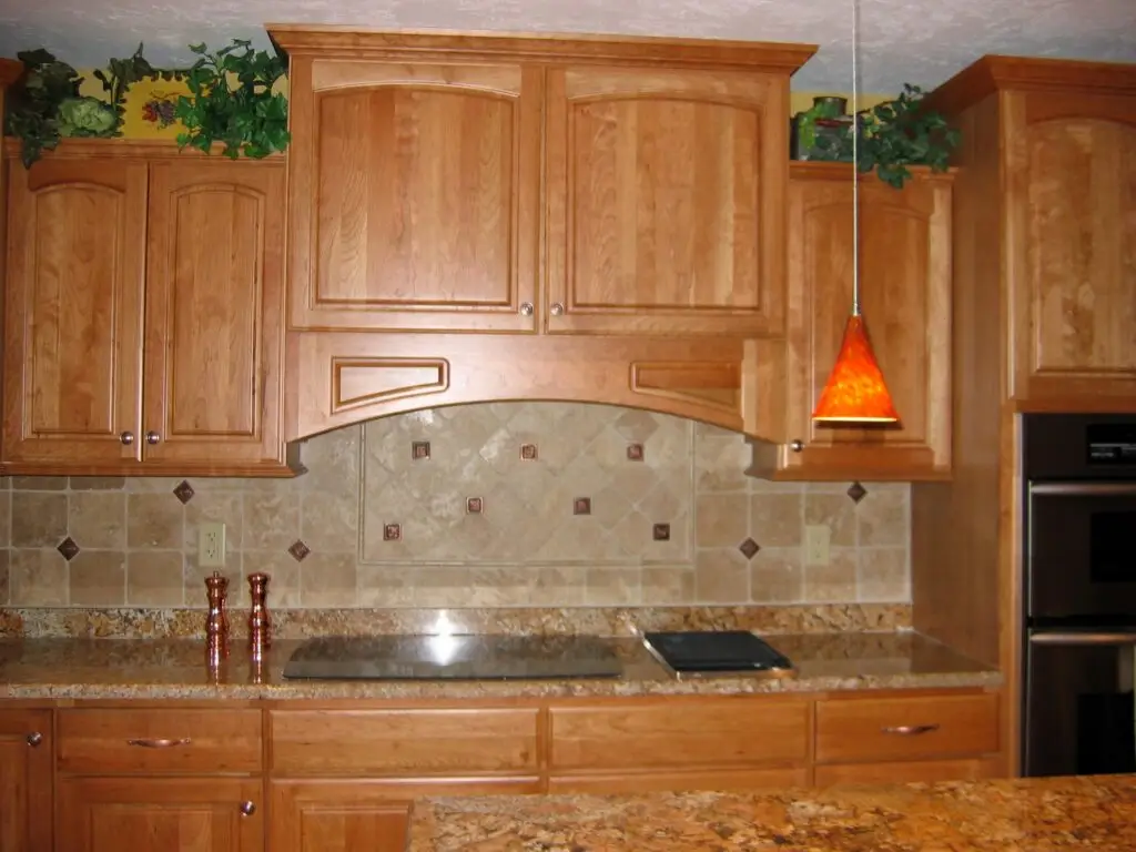 StarMark cherry cabinets and integrated wood hood over an induction cooktop with custom tile backsplash