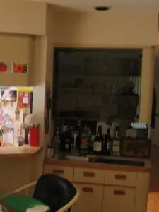 A dated 1980s wet bar with European-style almond cabinets and oak pulls, showing the before of a home bar remodel