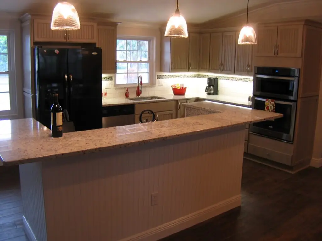 A neutral kitchen with beadboard doors, granite countertops and new appliances that are set off by the under cabinet lighting and 3 pendant lights over the island