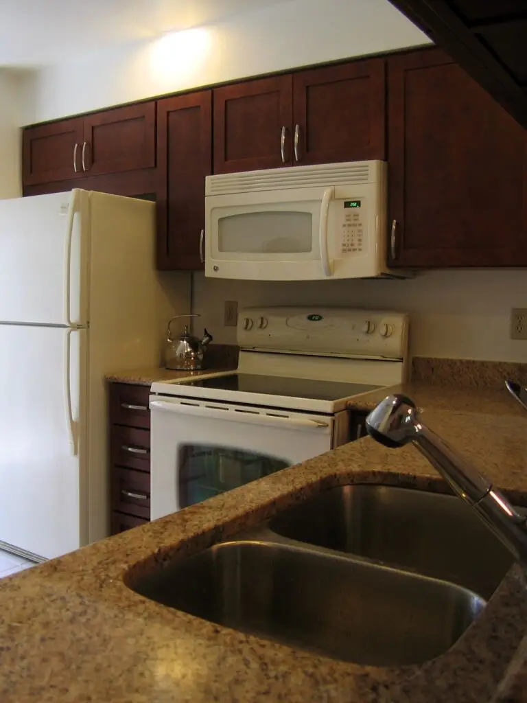Warm cabinets with a shaker door style and beige quartz countertops paired with bisque appliances and a stainless steel sink
