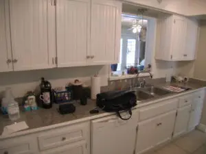 Before photo of tile countertops and worn, white cabinets