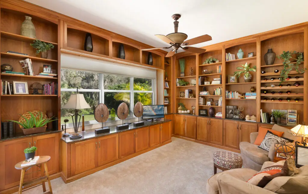 Bookcases featuring cherry cabinets and granite countertops highlight not only books but artwork, collections, and wine storage in this sunlit library specialty space for a recent River Woods project in Parrish.