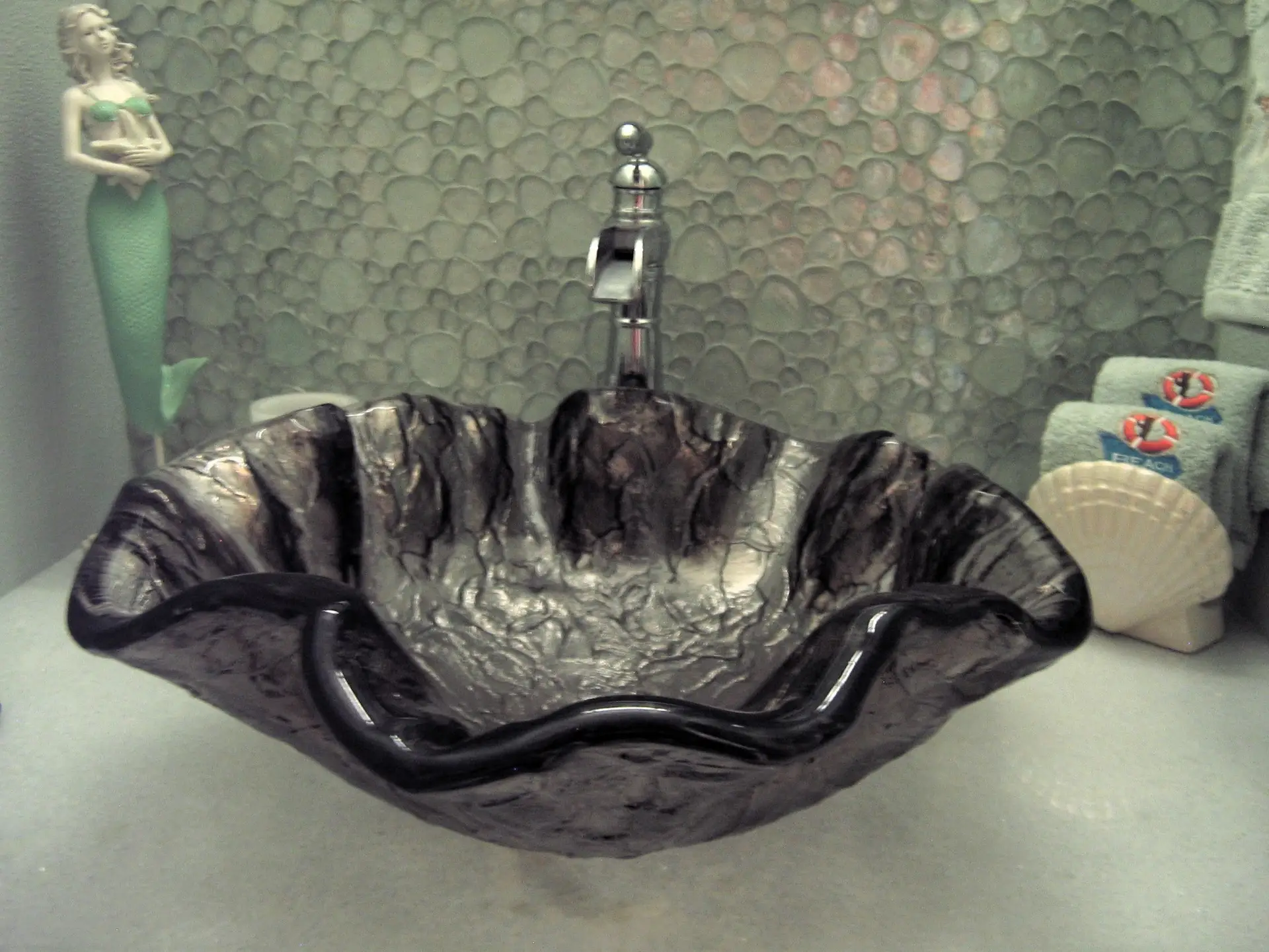 A custom bathroom design and remodel featuring a glass vessel sink in a free-form shell pattern for a powder room
