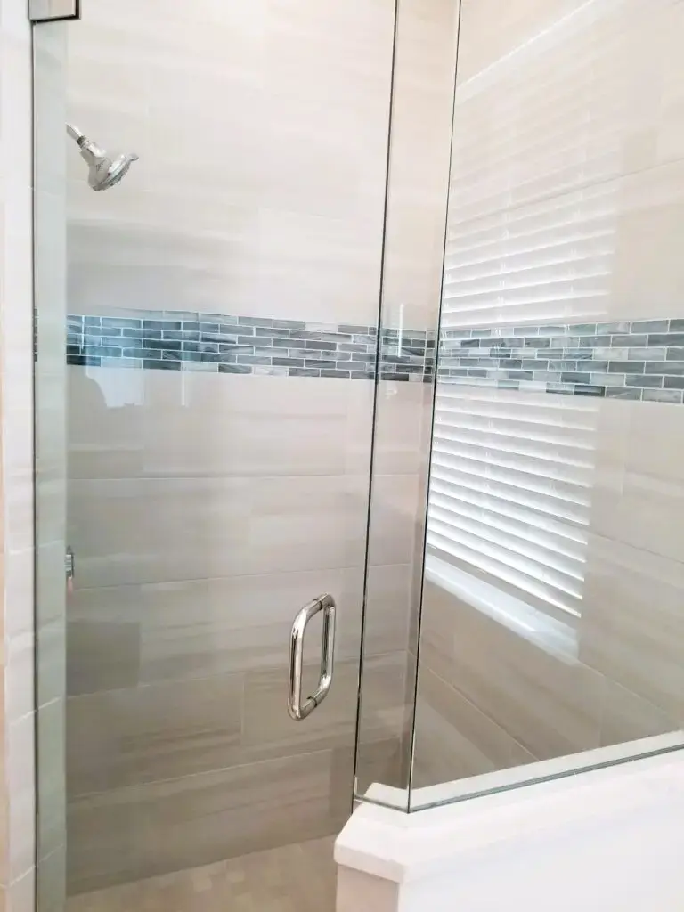Closeup of shower with clear glass enclosure along 12x24 wall tile featuring a navy blue accent band