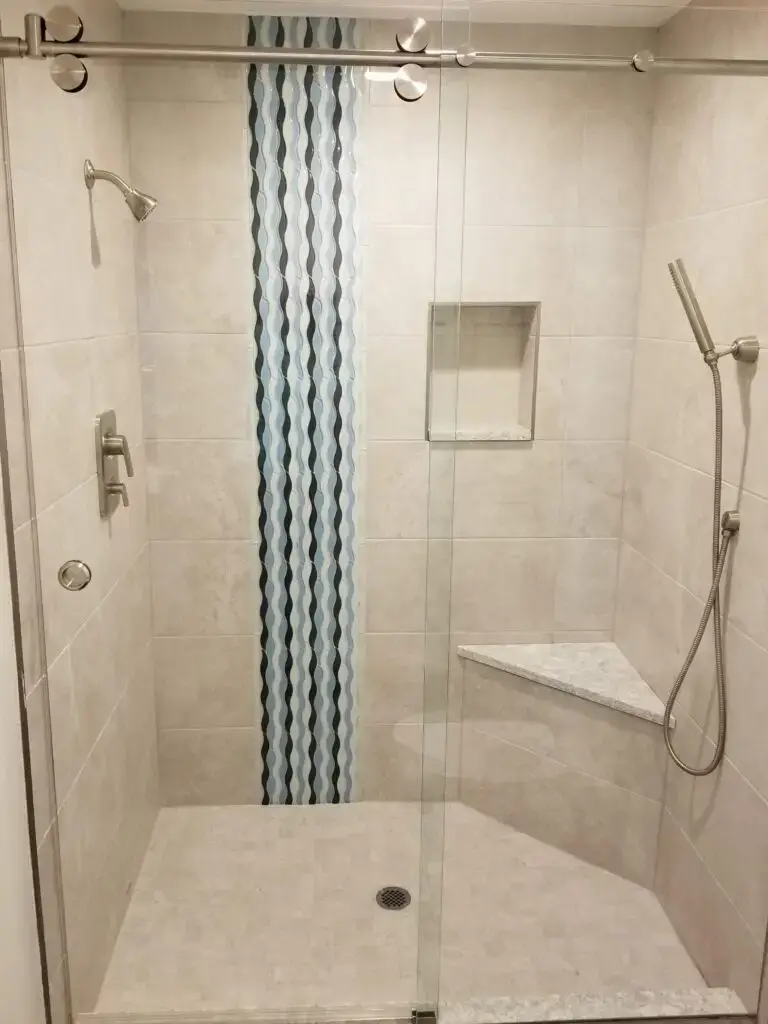A contemporary shower in a master bath remodel featuring a wavy blue glass tile accent and built in corner seat for aging in place