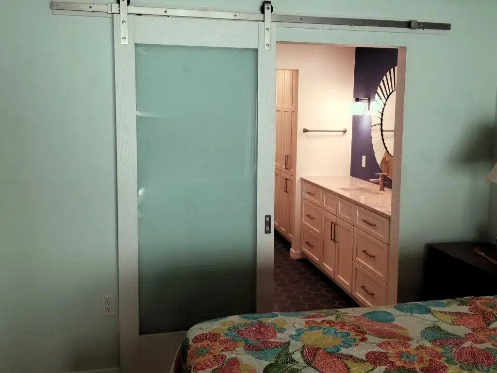 After – Vanity with sunburst mirror and royal blue accent wall beyond the frosted glass barn door for privacy