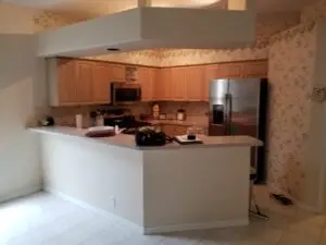 Before photo of outdated kitchen with wood cabinets and ivy wallpaper