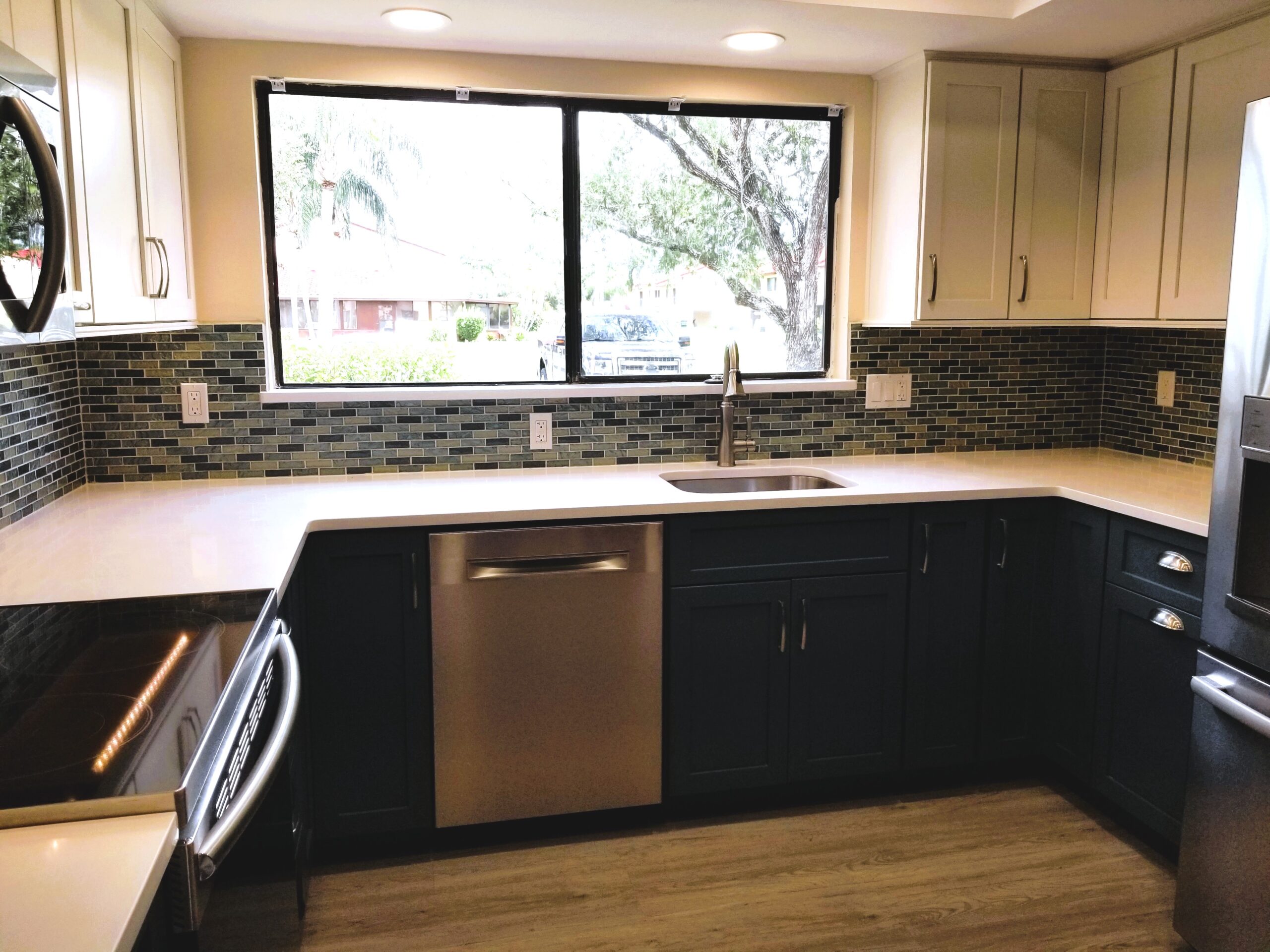 Modern kitchen sink and dishwasher area with a large window and two tone shaker cabinets