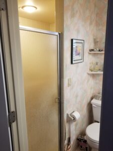 Outdated 1980s bathroom with enclosed shower wall and clutter